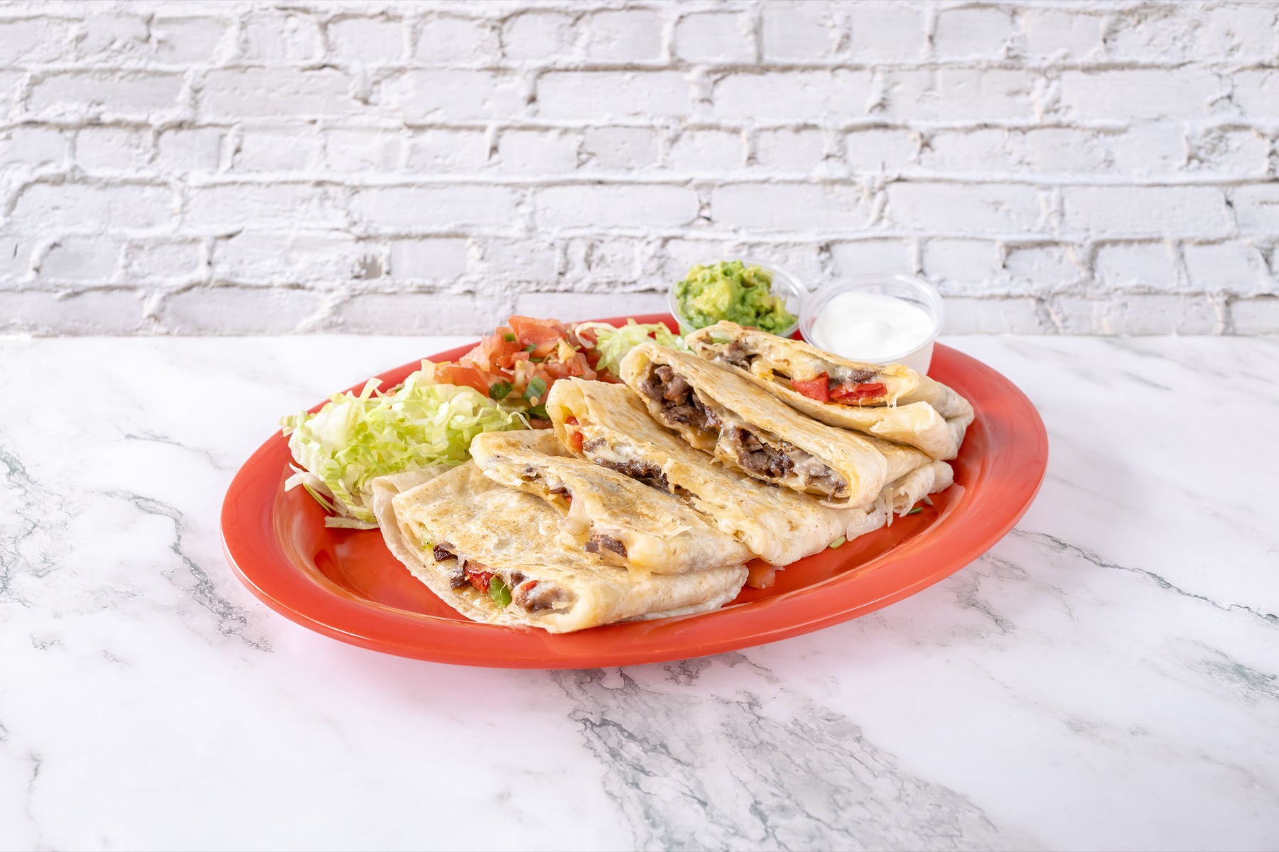 Asada quesadilla plate with lettuce, salsa, guacamole, and sour cream