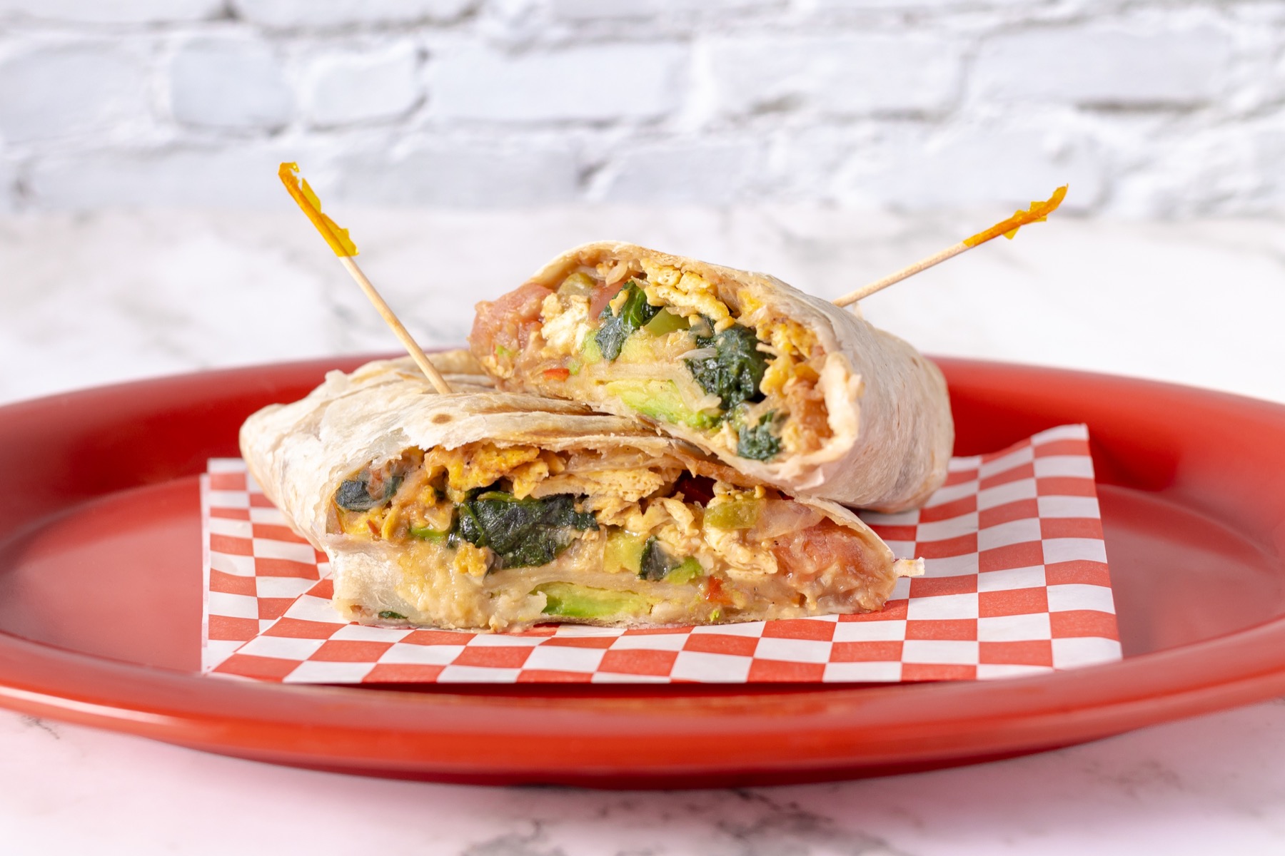 Breakfast wrap with eggs, greens, and avocado on checkered paper
