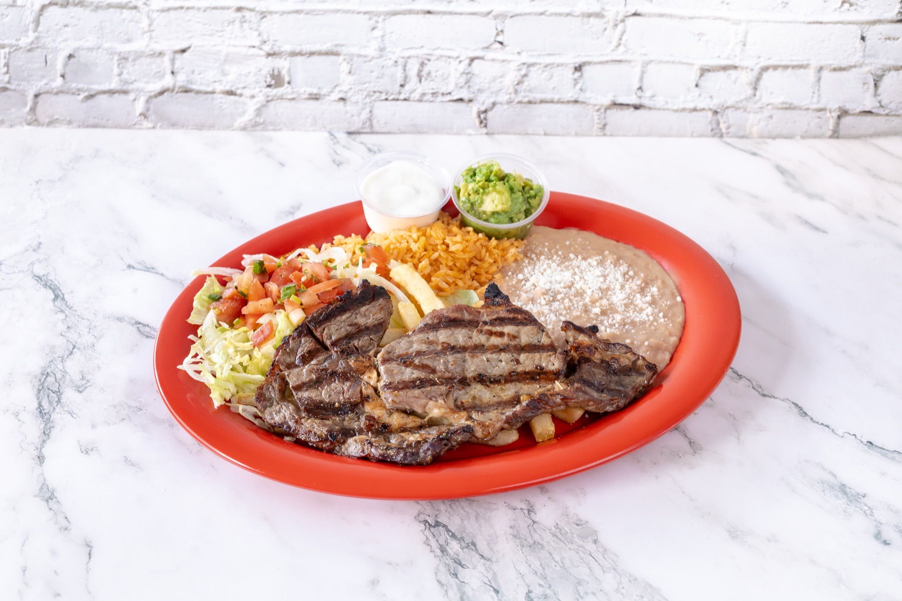 Carne asada plate with rice, beans, salad, guacamole, and sour cream