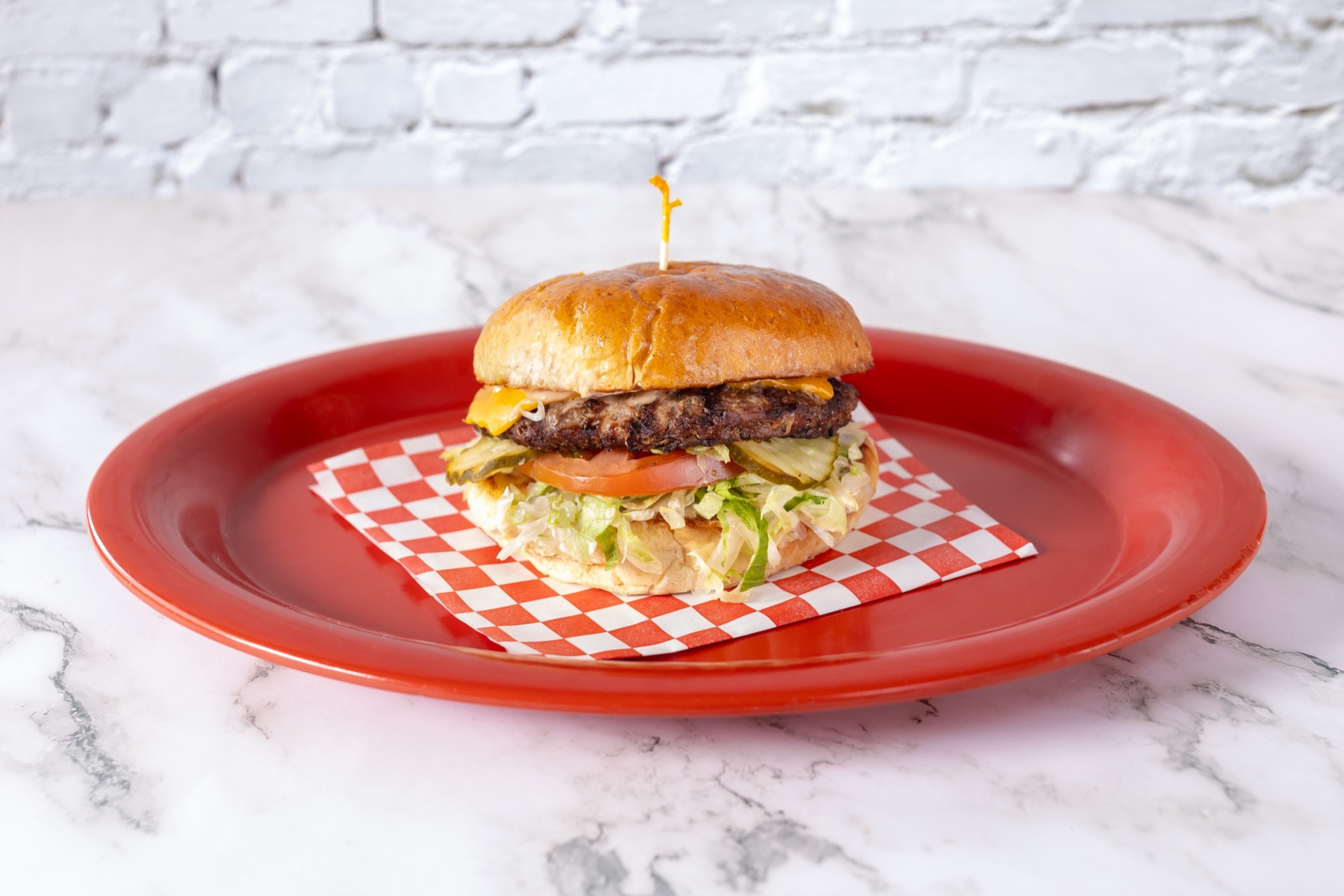 Cheeseburger with lettuce, pickles, and melted cheese on a red plate