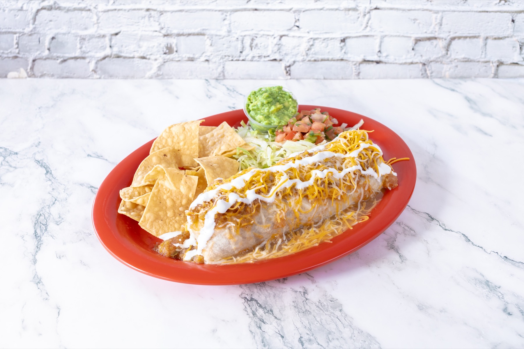 Wet burrito with cheese, sauce, chips, salad, and guacamole